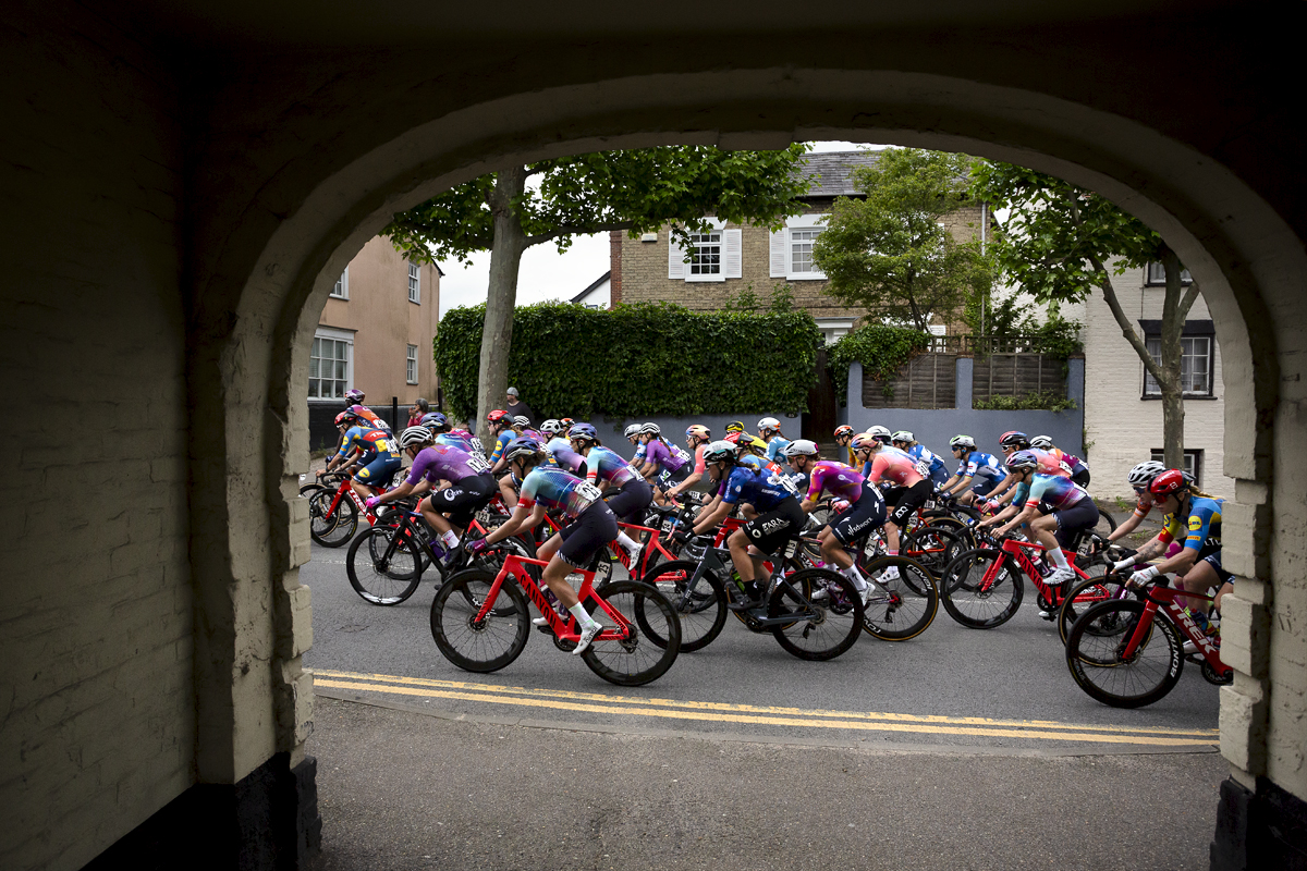 RideLondon Classique 2024 - The peloton seen through the entrance way of an old building