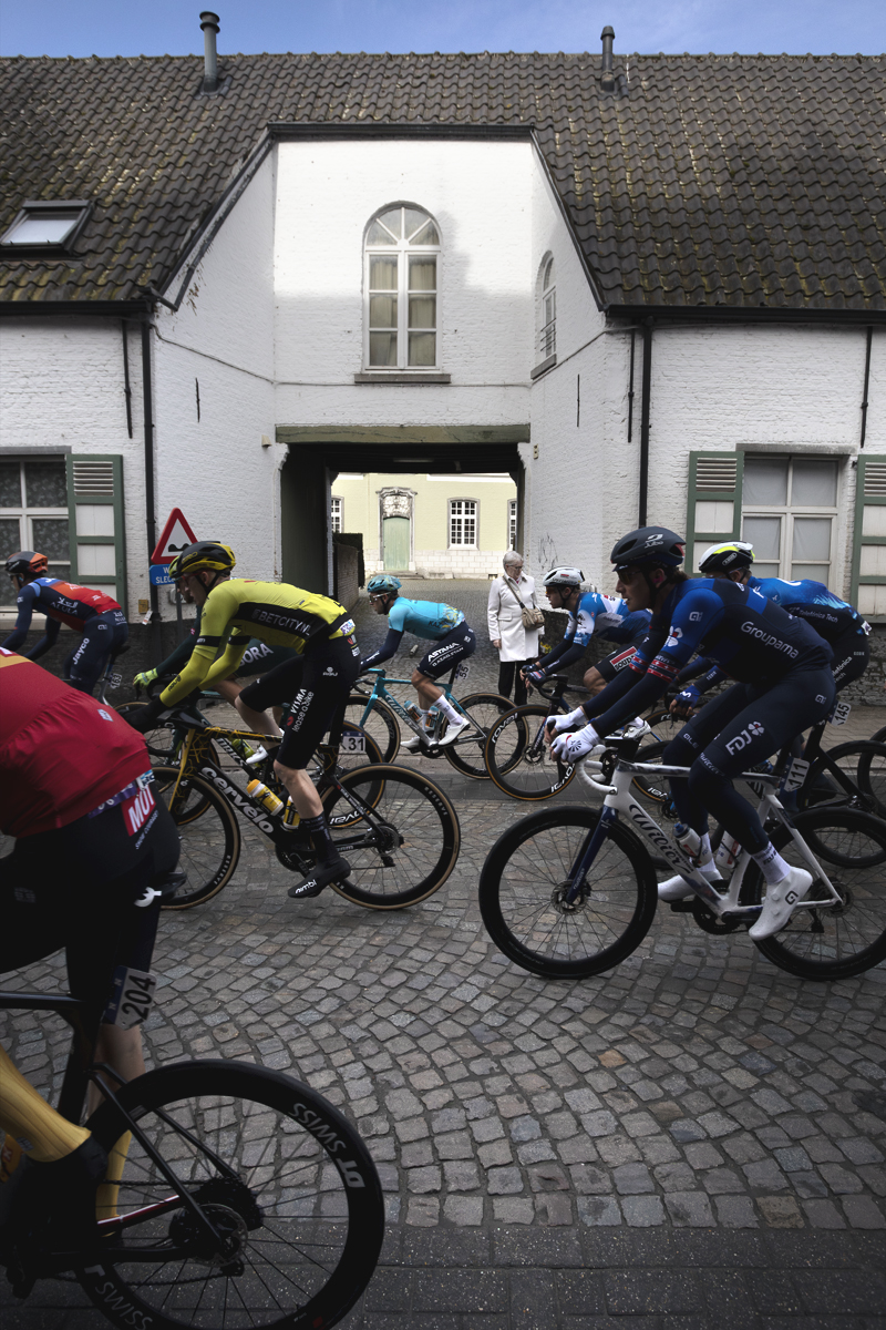 Ronde van Vlaanderen 2024 - Riders pass the gateway of a whitewashed building in Bazel