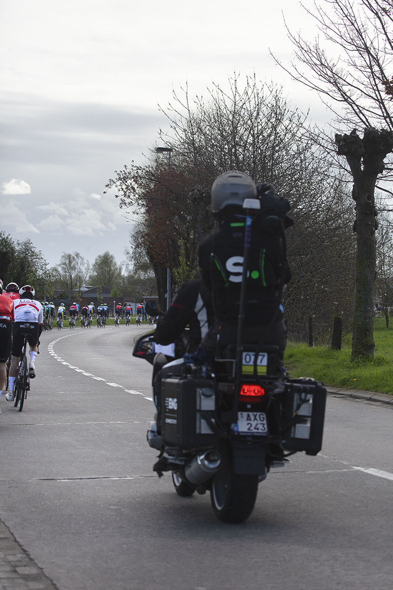 Ronde van Vlaanderen 2024 - The curve of the riders as they take a sweeping bend can be seen as the race is followed by a TV Moto