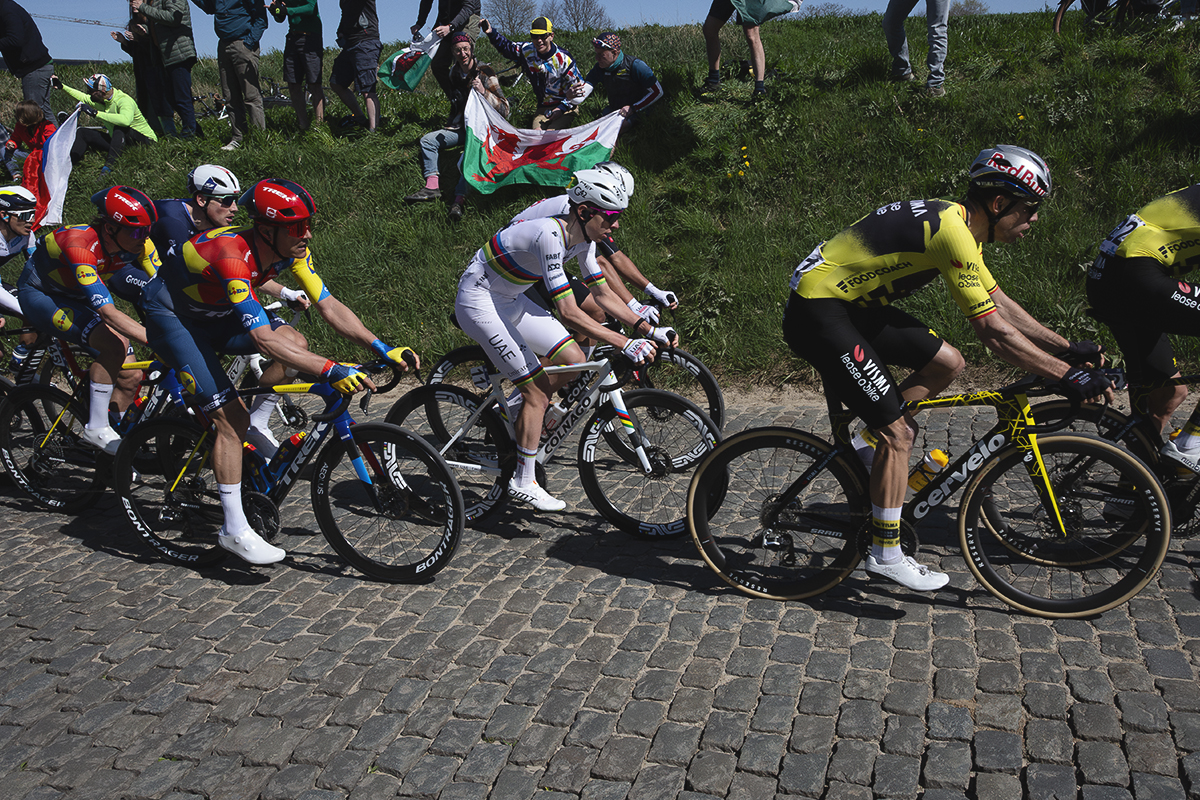 Ronde van Vlaanderen 2025 - A group of elite riders is cheered on by fans sitting on the high banks at the side of the road