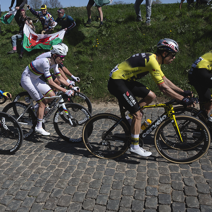 Ronde van Vlaanderen 2025 - A group of elite riders is cheered on by fans sitting on the high banks at the side of the road