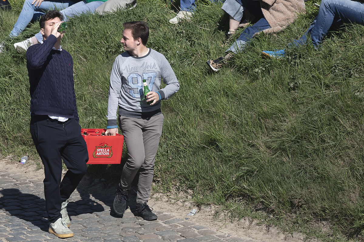 Ronde van Vlaanderen 2025 - Two young men carry a crate of Stella Artois and drink from bottles