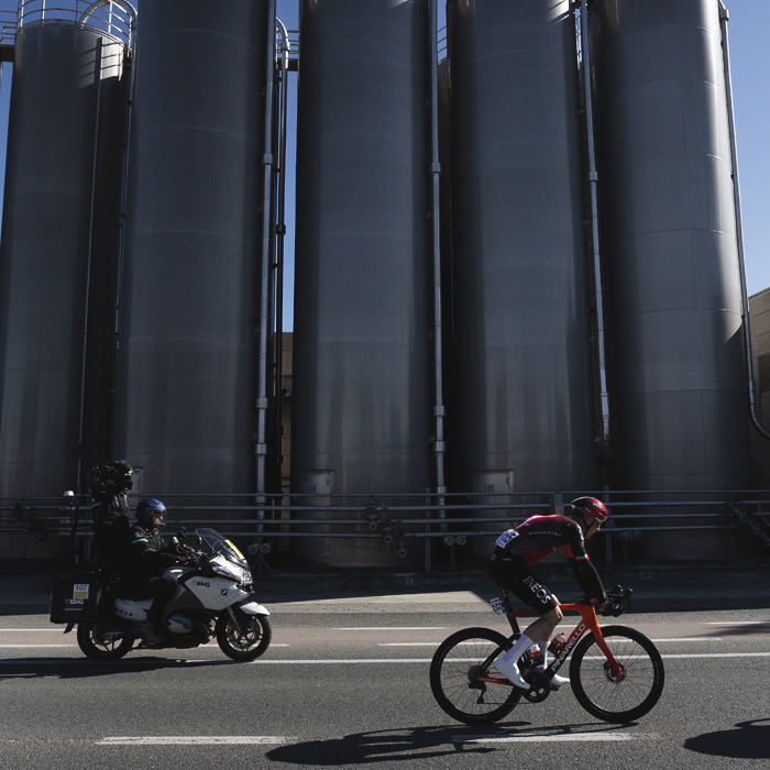 Ronde van Vlaanderen 2025 - Connor Swift rides past shiny industrial silos during the race