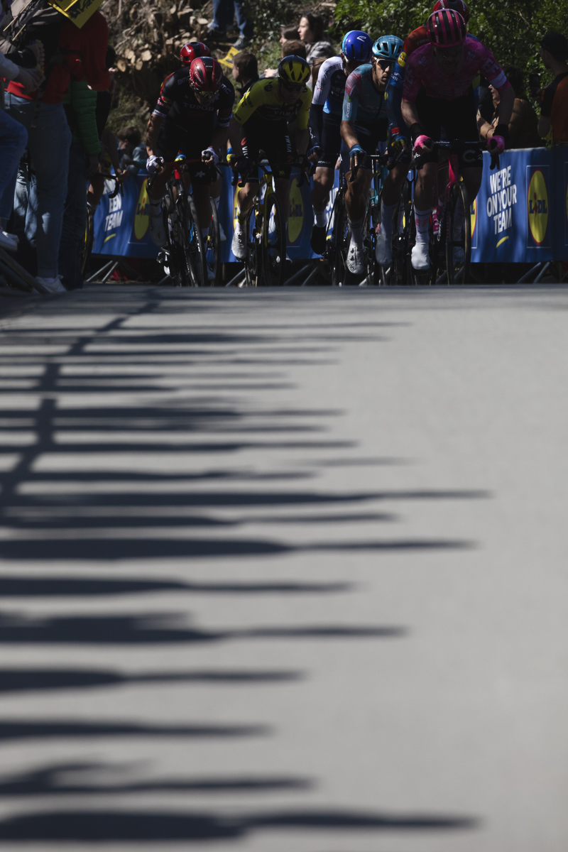 Ronde van Vlaanderen 2025 - Davide Toneatti leads a group of riders up a climb with the shadows of waiting fans cast onto the road