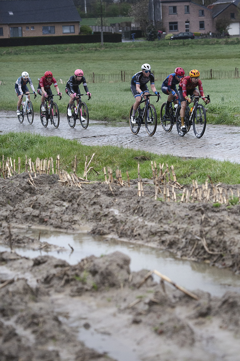 Ronde van Vlaanderen Vrouwen 2024 - A group of riders viewed across waterlogged furrows on Mariaborrestraat