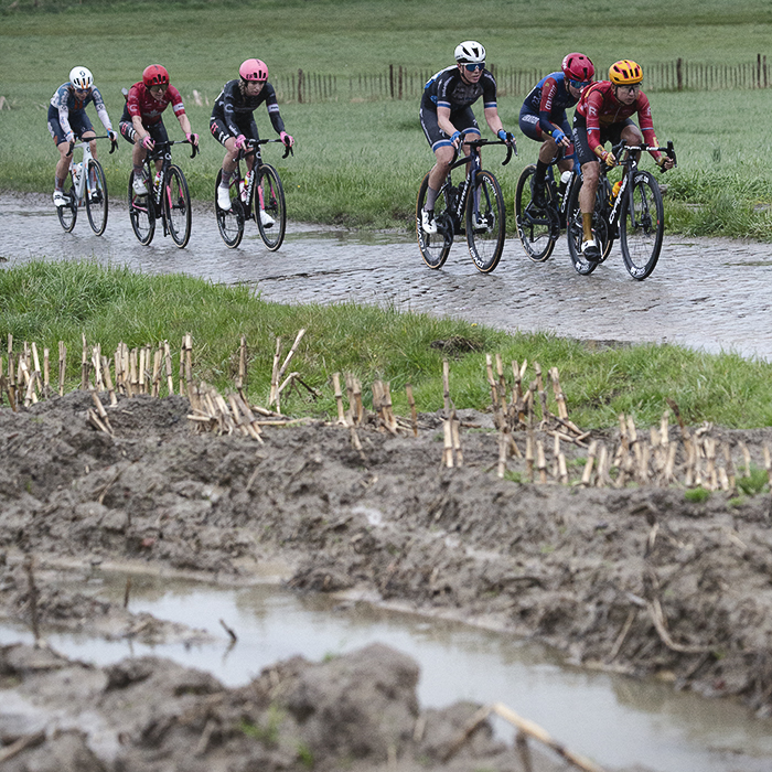 Ronde van Vlaanderen Vrouwen 2024 - A group of riders viewed across waterlogged furrows on Mariaborrestraat