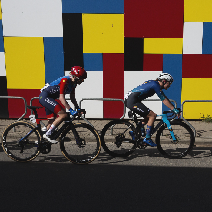 Ronde van Vlaanderen Vrouwen 2025 - Riders pass a brightly coloured, Mondrian style wall Michelbeke