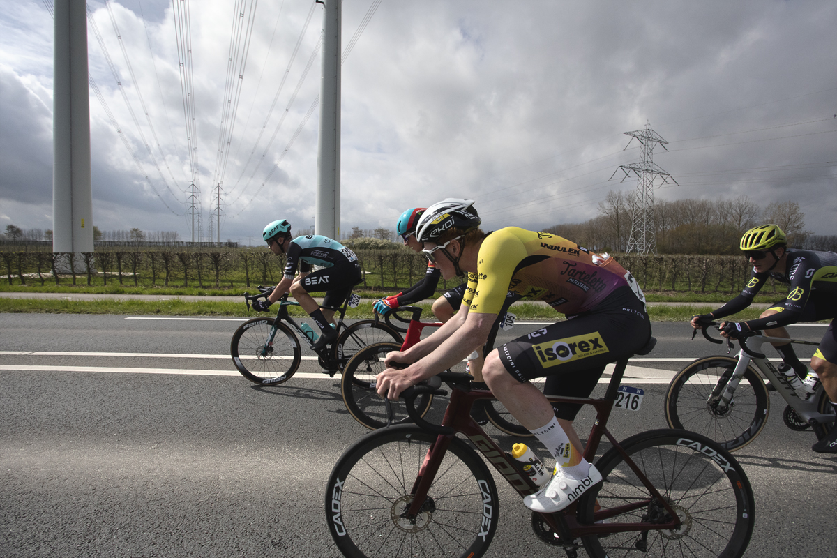 Scheldeprijs 2024 - A group of riders pass under modern pylons near Heinkenszand