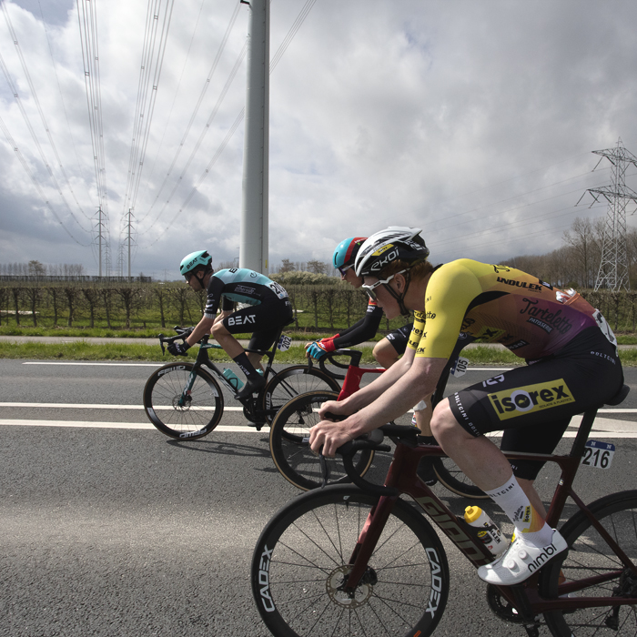 Scheldeprijs 2024 - A group of riders pass under modern pylons near Heinkenszand