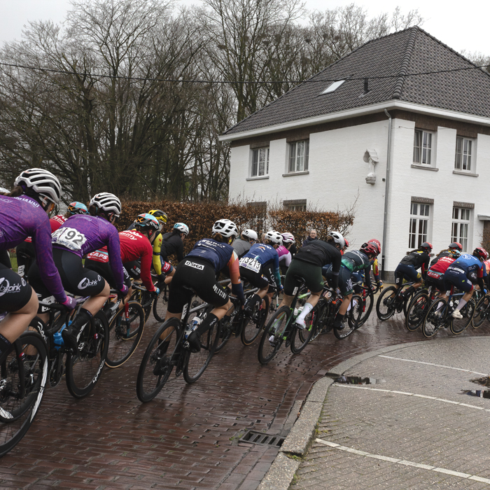 Scheldeprijs Vrouwen 2024 - Riders pass in fort of a white building in Achterbroek