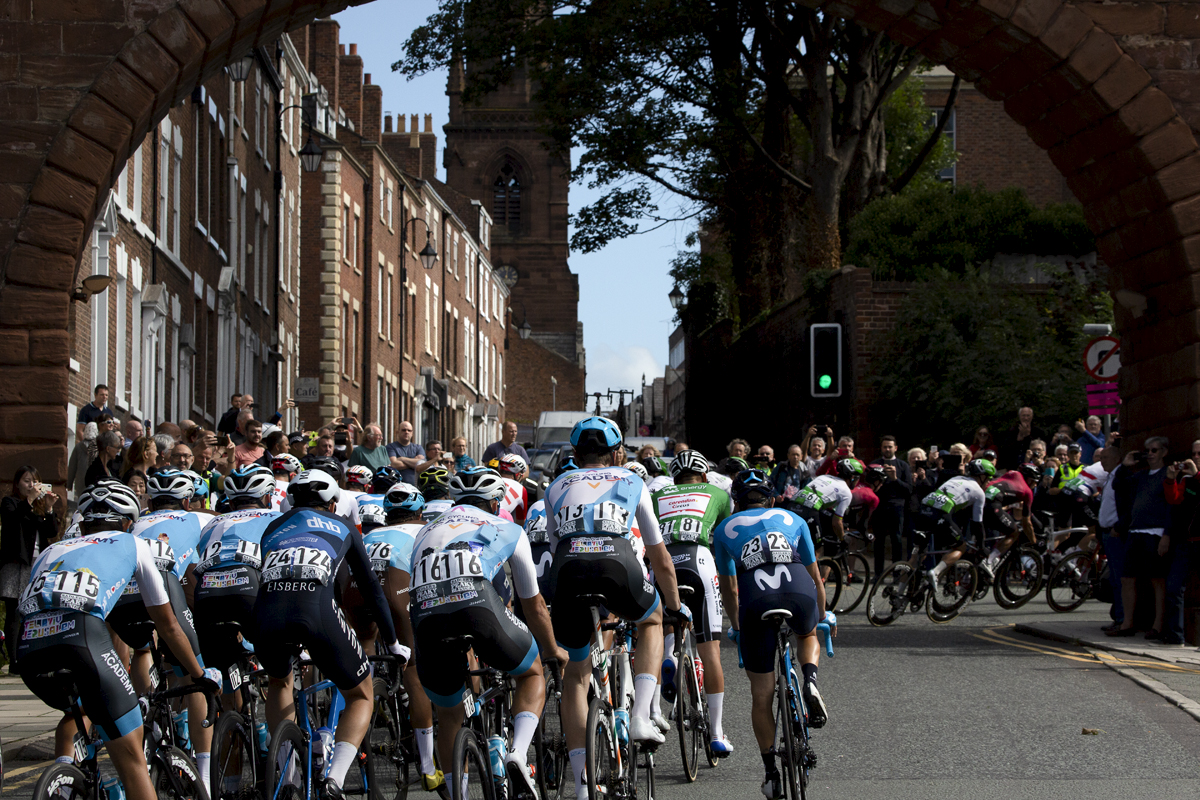 Tour of Britain 2019 - rear view of the  peloton passing under one of the gates in the walls in Chester