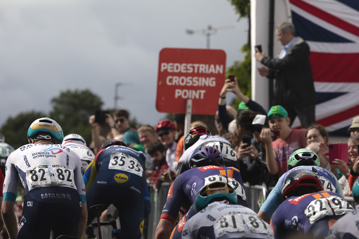 Tour of Britain 2025 - Spectators film the race on their phones with a Union flag as a backdrop
