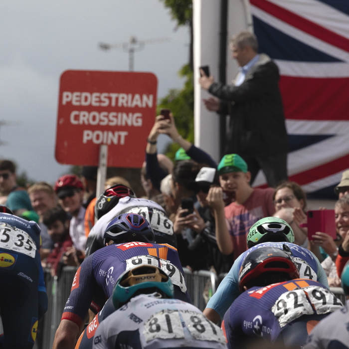 Tour of Britain 2025 - Spectators film the race on their phones with a Union flag as a backdrop