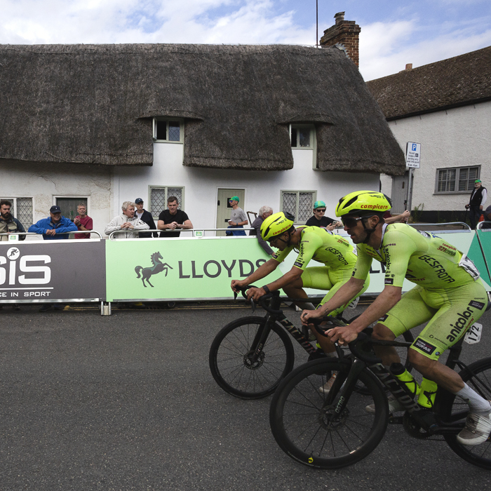 Tour of Britain 2025 - Alexis Guerin & Paulo Fernandes ride in front of a white thatched cottage
