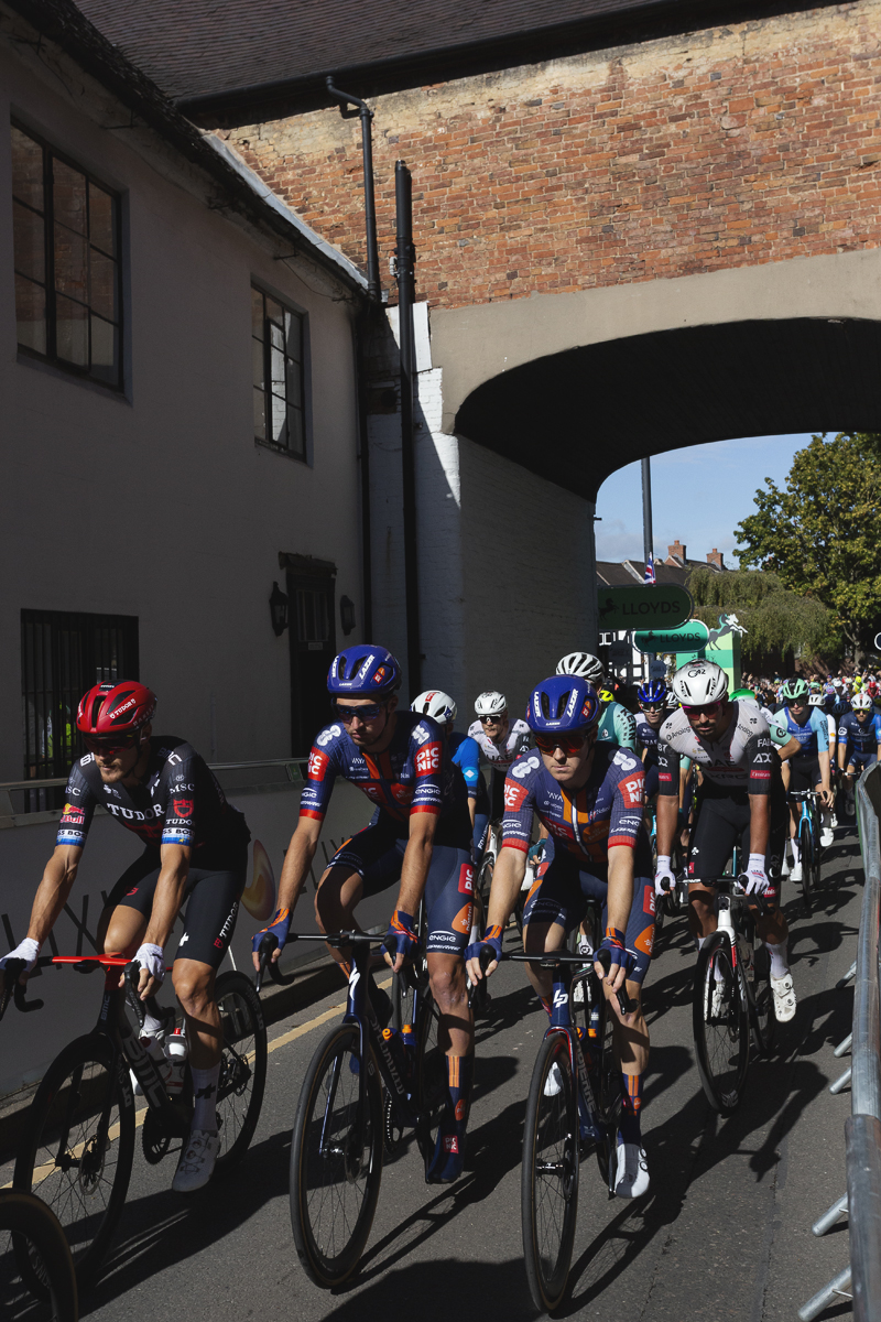 Tour of Britain 2025 - The peloton rolls out through an archway in Atherstone
