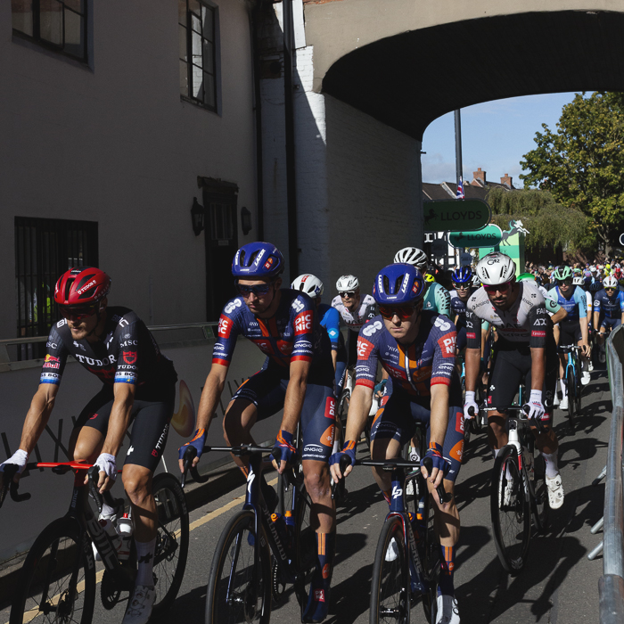 Tour of Britain 2025 - The peloton rolls out through an archway in Atherstone