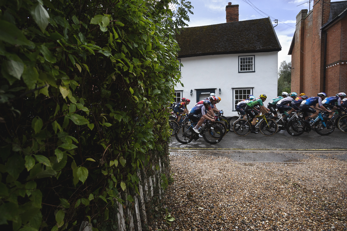Tour of Britain 2025 - The peloton passes in front of a white cottage in Bildeston