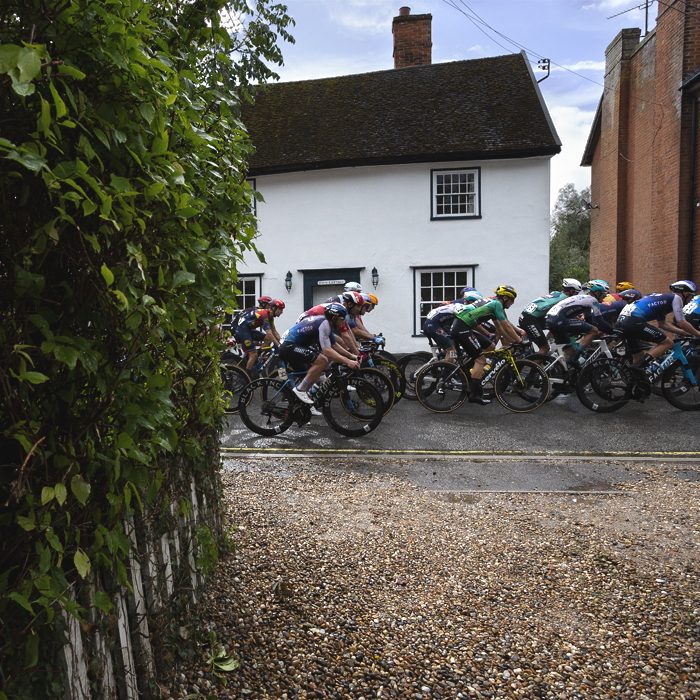 Tour of Britain 2025 - The peloton passes in front of a white cottage in Bildeston