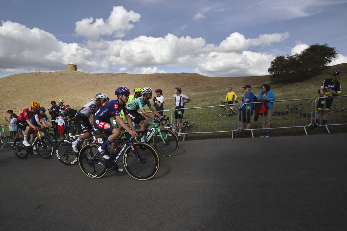 Tour of Britain 2025 - Fans cheer on a group of riders with a small squat tower seen on a distant hill at Burton Dassett
