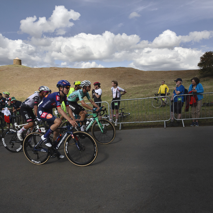 Tour of Britain 2025 - Fans cheer on a group of riders with a small squat tower seen on a distant hill at Burton Dassett