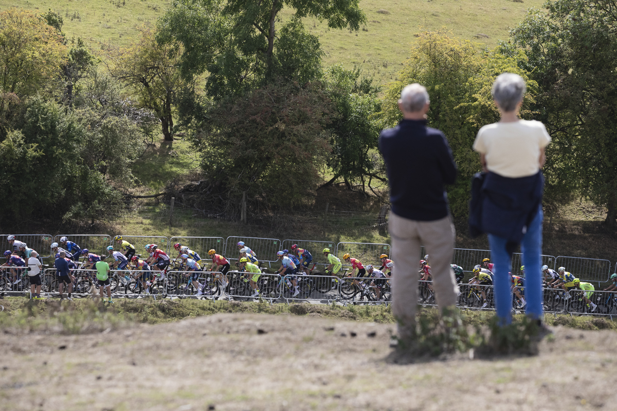 Tour of Britain 2025 - The race is framed by two spectators as it begins to climb the hill at Burton Dassett