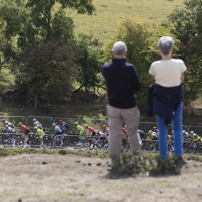 Tour of Britain 2025 - The race is framed by two spectators as it begins to climb the hill at Burton Dassett