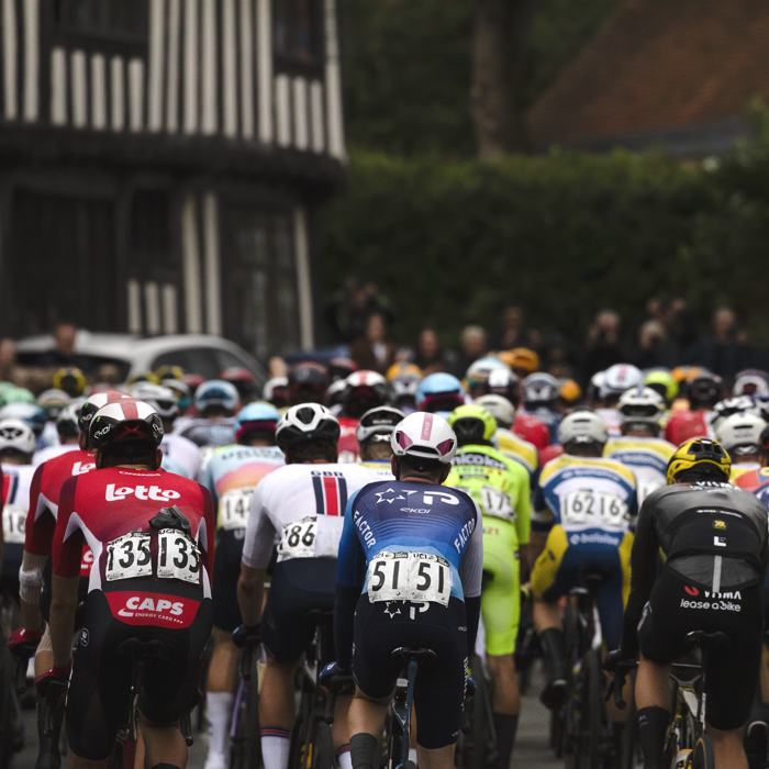Tour of Britain 2025 - A rear view of riders passing timber framed buildings in Lavenham