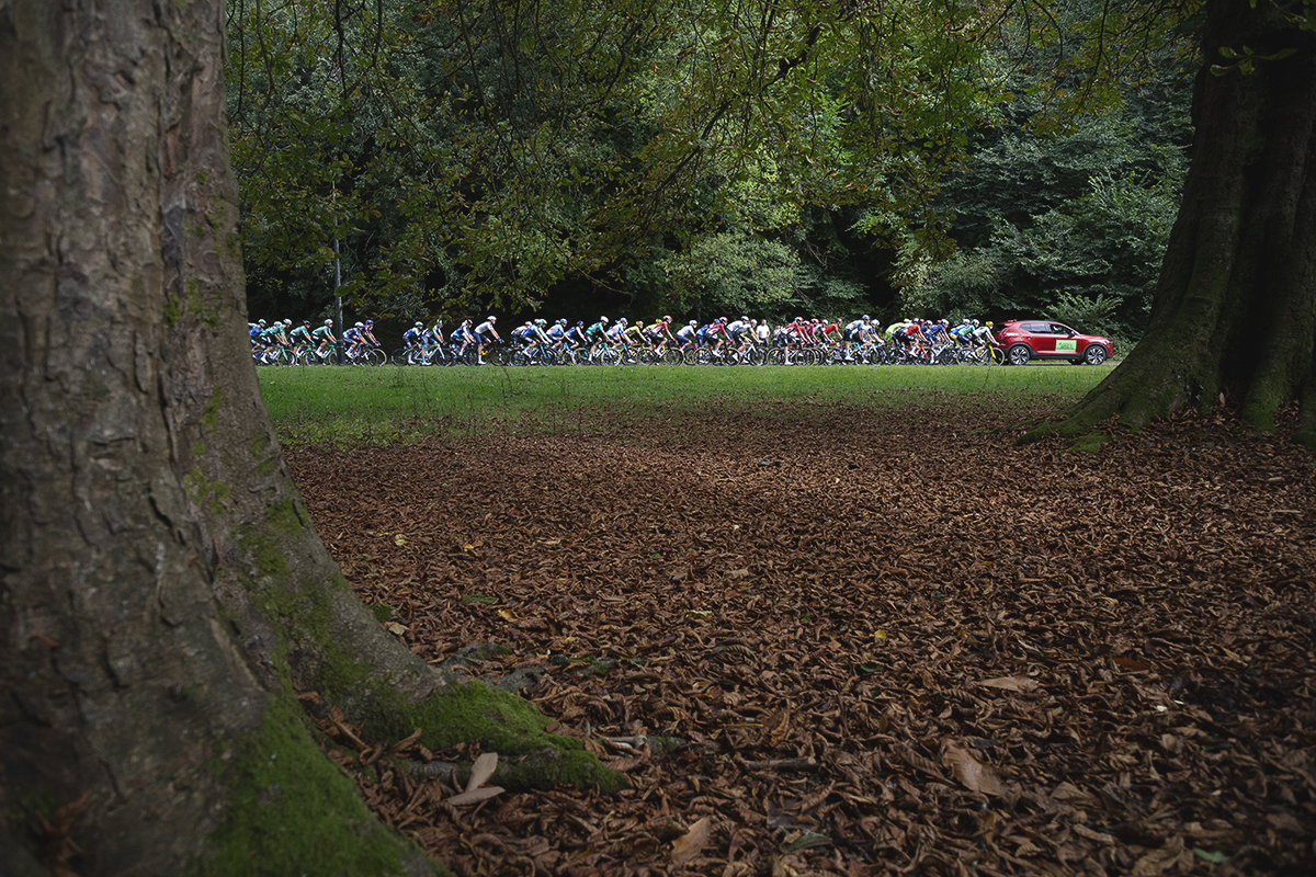 Tour of Britain 2025 - Fallen leaves lie on the ground next to mature trees as the peloton is led through Pontypool Park by the red Race Director’s car