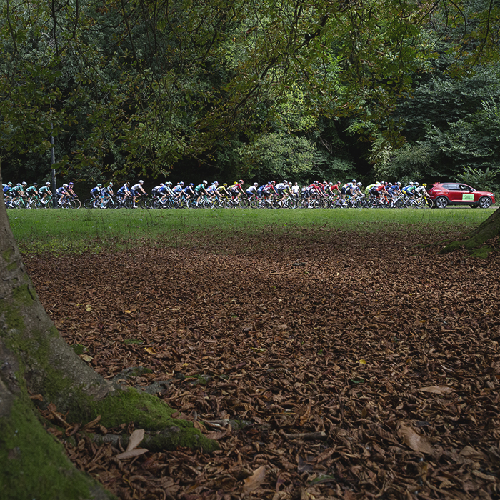 Tour of Britain 2025 - Fallen leaves lie on the ground next to mature trees as the peloton is led through Pontypool Park by the red Race Director’s car