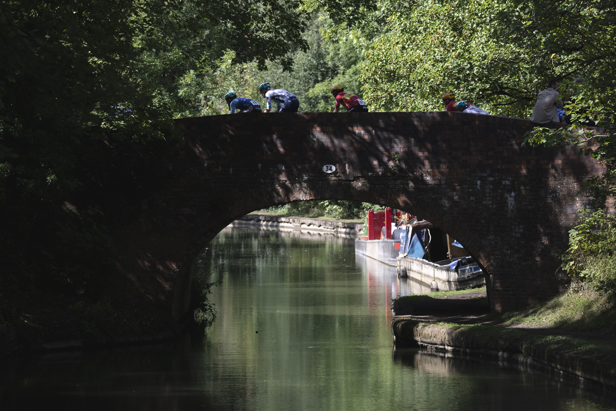 Tour of Britain 2025 - A group of riders pass over a canal bridge with narrow boats in the background