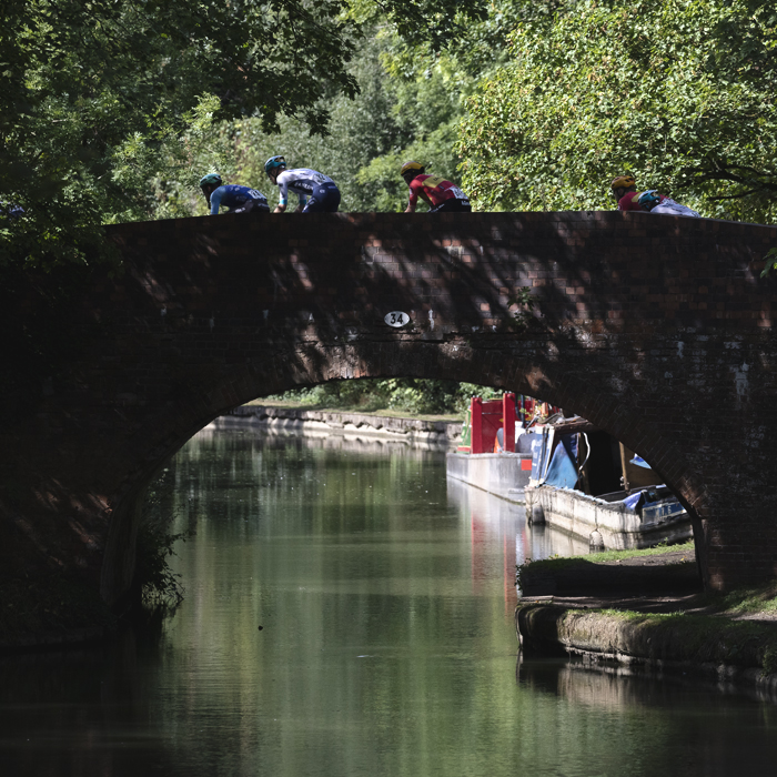 Tour of Britain 2025 - A group of riders pass over a canal bridge with narrow boats in the background