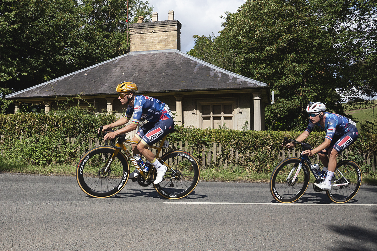 Tour of Britain 2025 - Remco Evenepoel and Ethan Hayter ride past a stone gate house