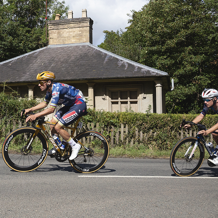 Tour of Britain 2025 - Remco Evenepoel and Ethan Hayter ride past a stone gate house