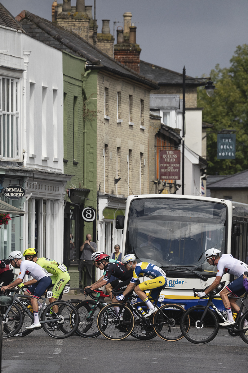 Tour of Britain 2025 - Riders cross a junction in Saxmundham while a local bus service is held up by the race