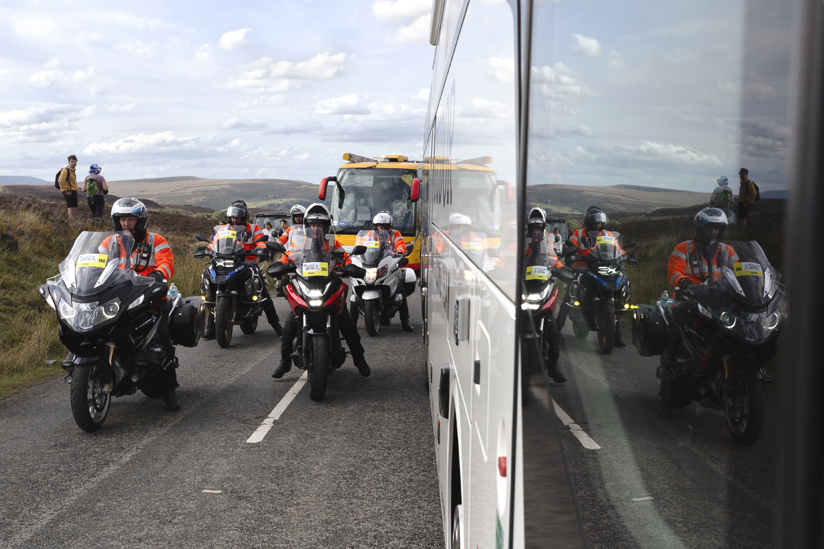 Tour of Britain 2025 - Motorcycle outriders are reflected in the side of the team buses