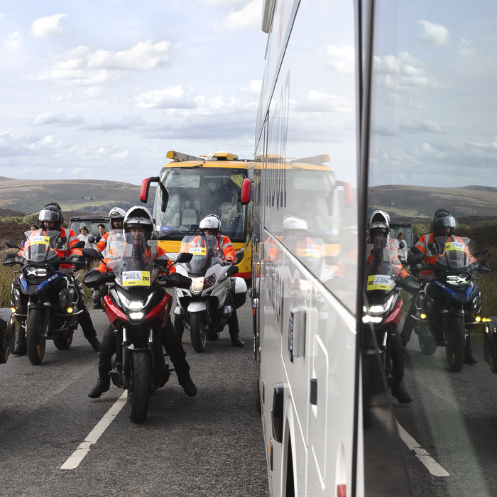Tour of Britain 2025 - Motorcycle outriders are reflected in the side of the team buses