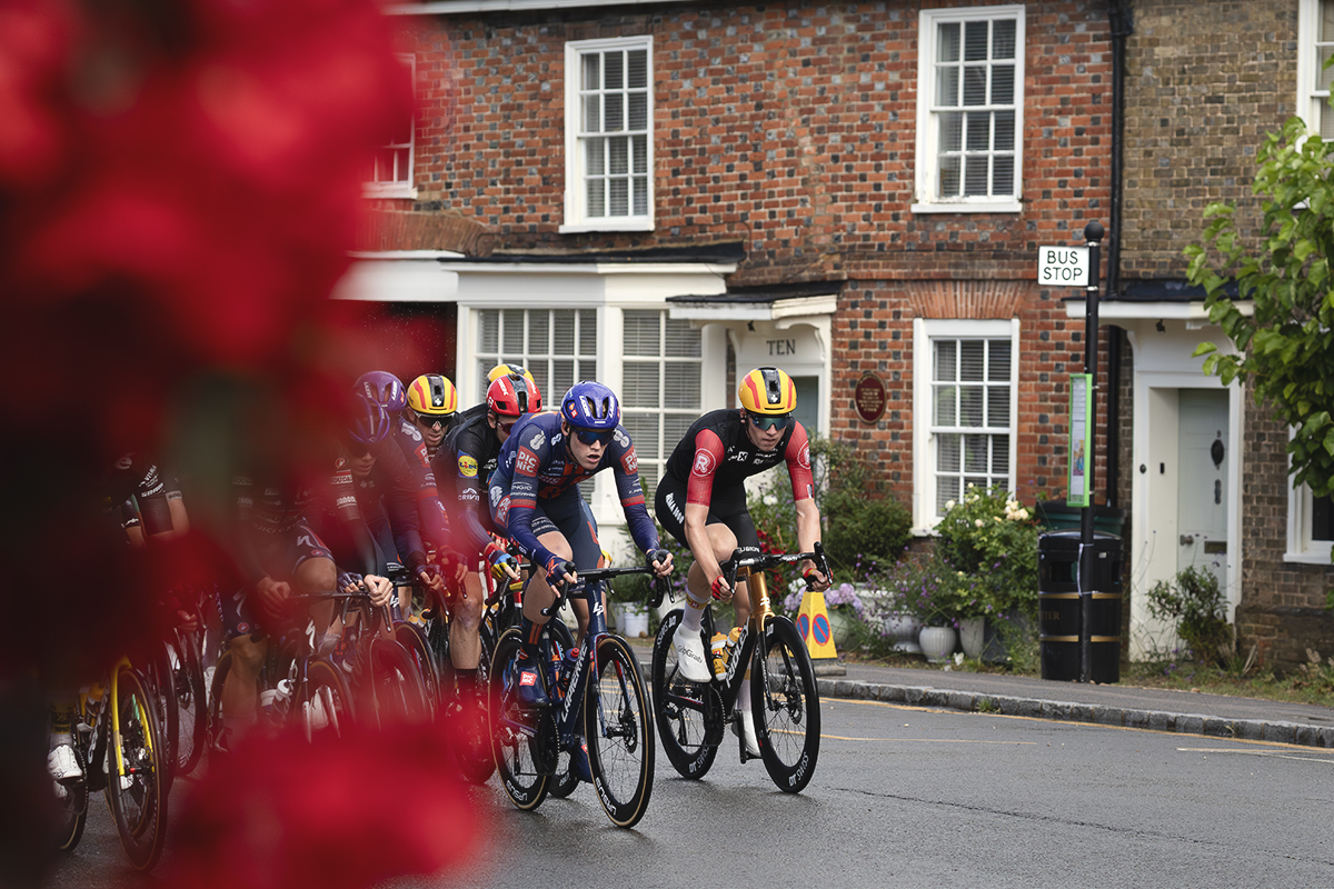 Tour of Britain 2025 - A hanging basket frames the riders in the High Street of Woburn