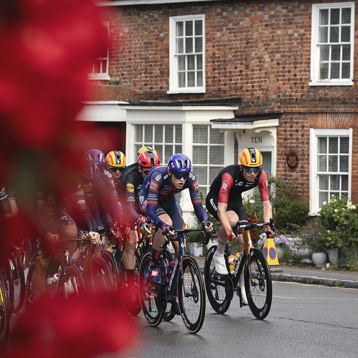 Tour of Britain 2025 - A hanging basket frames the riders in the High Street of Woburn
