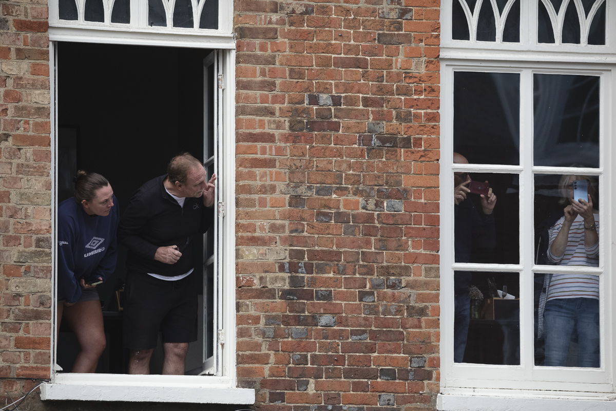 Tour of Britain 2025 - Spectators lean out of upper floor windows to get a view of the race