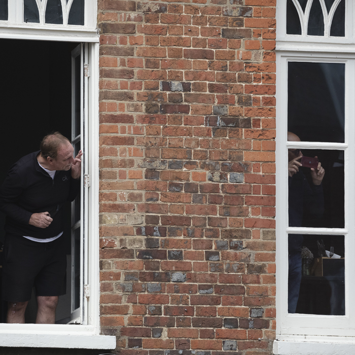 Tour of Britain 2025 - Spectators lean out of upper floor windows to get a view of the race