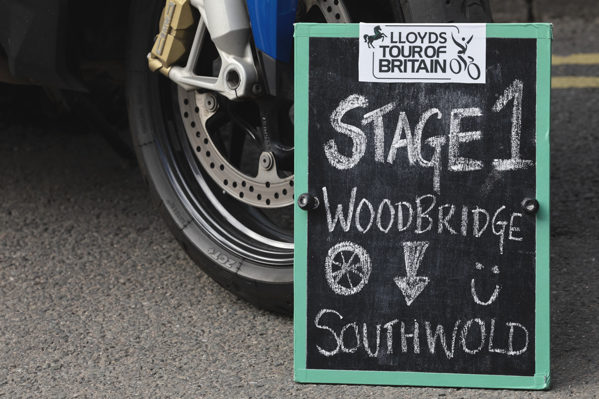 Tour of Britain 2025 - A blackboard next to a motorcycle wheel welcomes spectators to Woodbridge at the start of the race