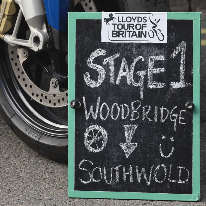 Tour of Britain 2025 - A blackboard next to a motorcycle wheel welcomes spectators to Woodbridge at the start of the race