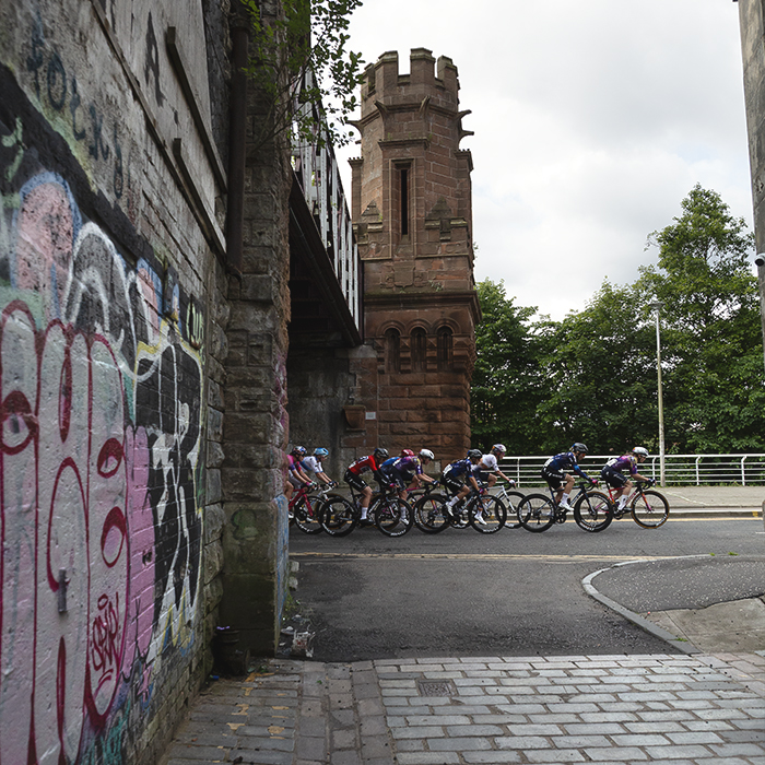 Tour of Britain Women’s 2025 - Stage 4 - The peloton on Clyde Street as seen from Merchant Lane  with grafitti in the foreground
