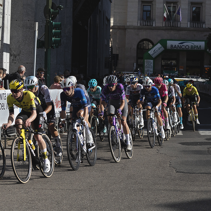 Tre Valli Varesine 2025 - Riders pass by commercial buildings in Varese