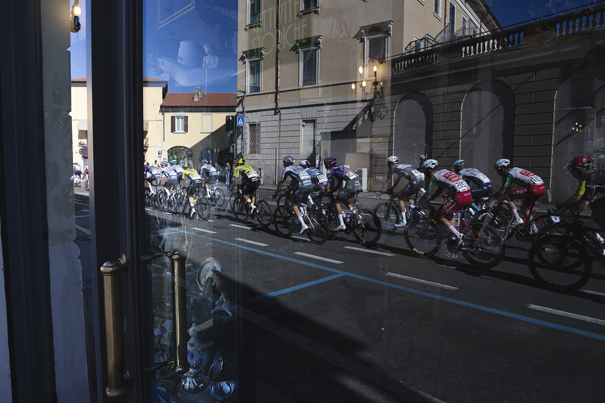 Tre Valli Varesine 2025 - The peloton is reflected in the window of an antiques shop