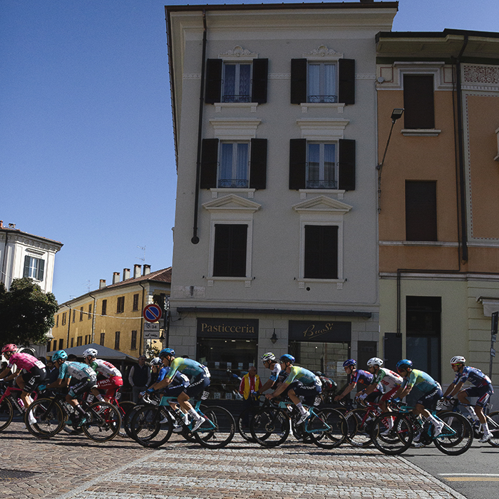 Tre Valli Varesine 2025 - Riders cross over a zebra crossing built into te brickwork of the road surface in front of Pasticceria Buosi