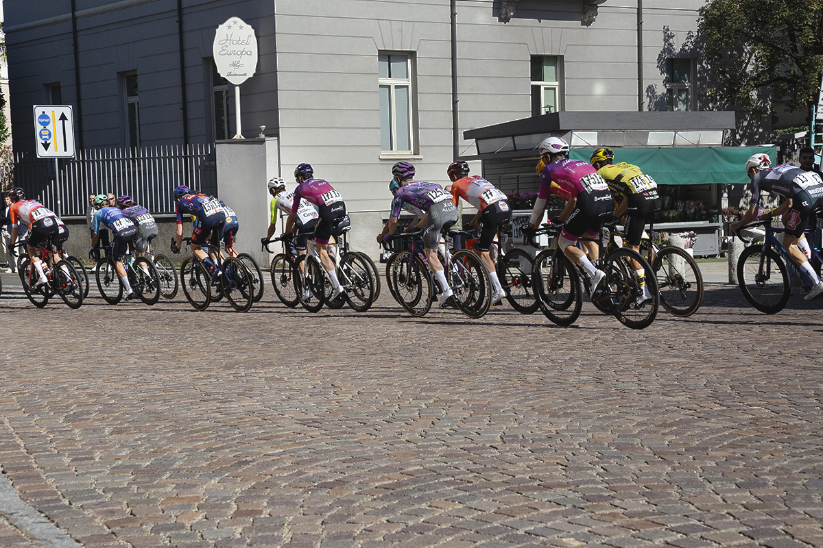 Tre Valli Varesine 2025 - The peloton seen riding over ornate cobbles in the centre of Varese