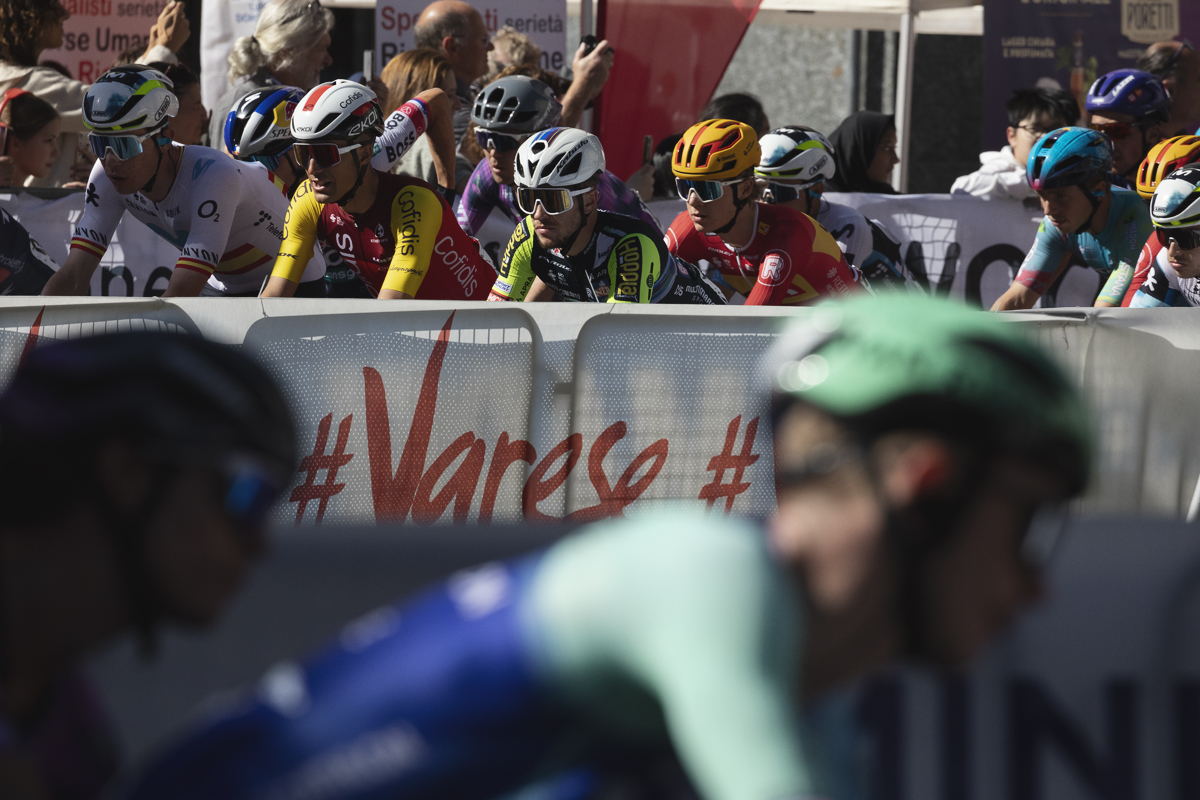 Tre Valli Varesine 2025 - Riders pass by an advertising hoarding bearing the word Varese