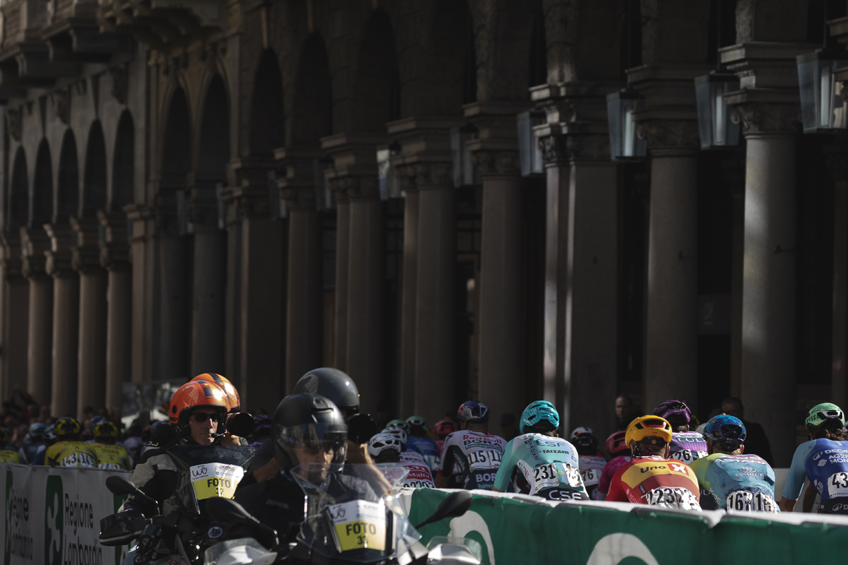 Tre Valli Varesine 2025 - The columns of an arcade are seen in the background as riders pass through the city as the moto photographers watch on