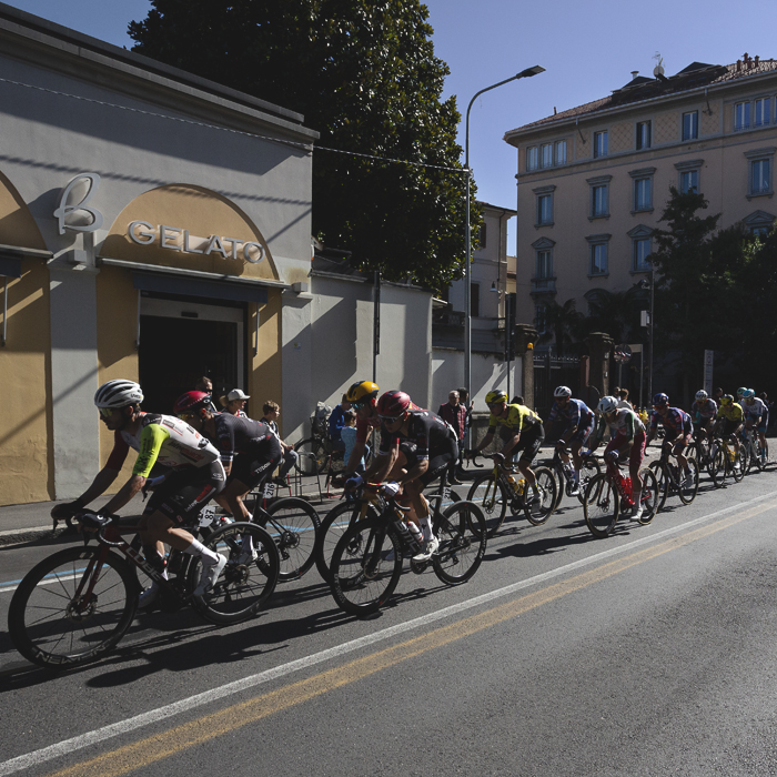 Tre Valli Varesine 2025 - The peloton passes by a gelato shop in central Varese